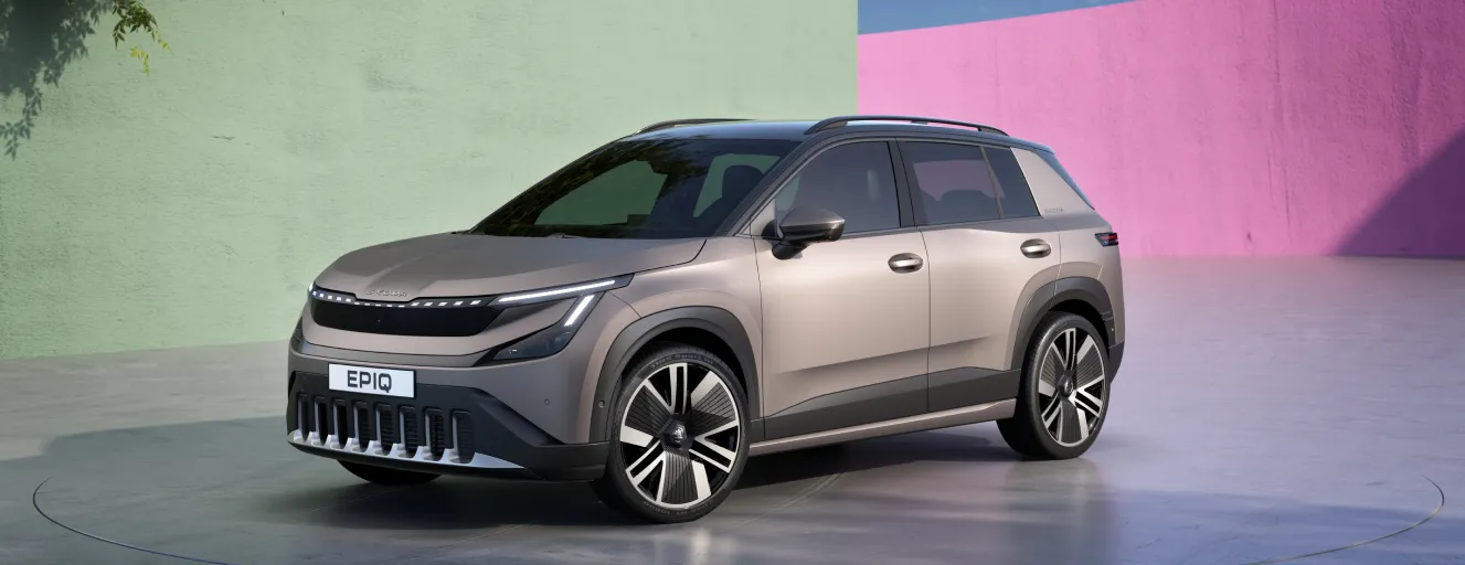 A modern Skoda Elroq electric SUV in a champagne silver finish, parked in a bright, colorful studio.